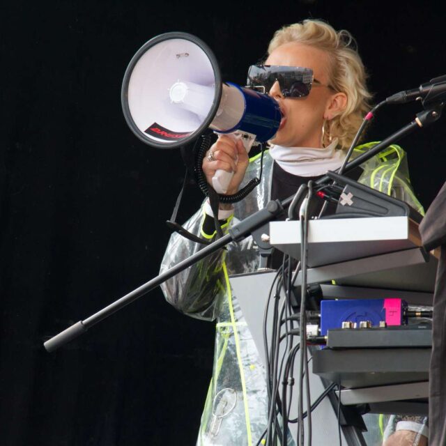 Ung kvinna i solglasögon talar i megafon på en scen.