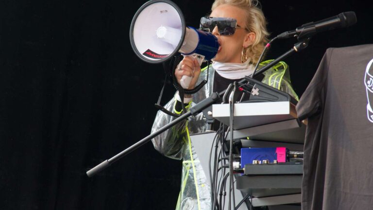 Ung kvinna i solglasögon talar i megafon på en scen.