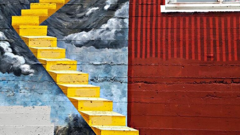 Konstinstallation med en gul trappa som går upp till ett hål i en vägg.