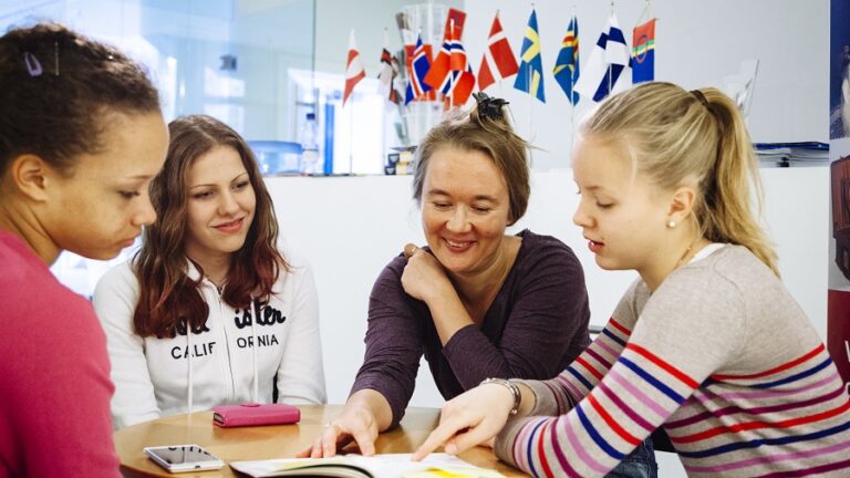 Four girls sitting at a round table reading, in the background all the Nordic flags.