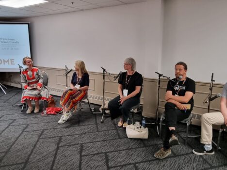 A panel of two woman and three men in a meeting room, the interviewer wears a Sámi dress.