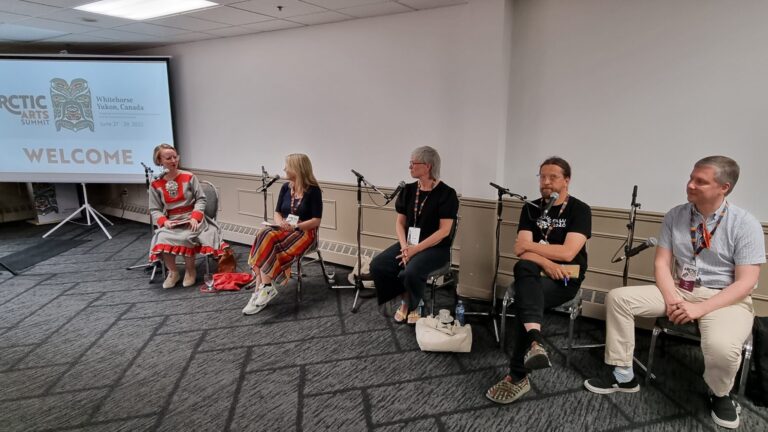 A panel of two woman and three men in a meeting room, the interviewer wears a Sámi dress.