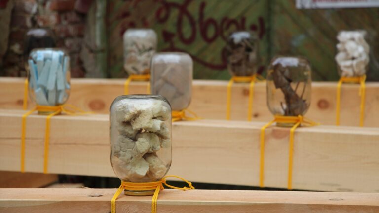 Konstinstallation med fyllda glasburkar på träplankor.