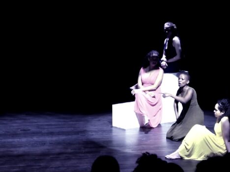 Actresses in long dresses sitting in the spotlight on a dark stage