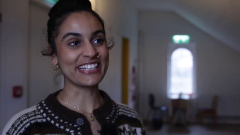 Taiteilija Nayab Ikram hymyilee kameralle, taustalla ikkuna.