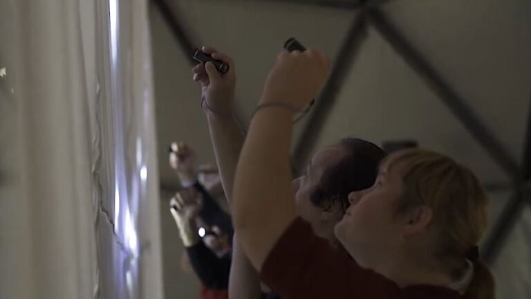 People pointing flashlights against a white sheet in order to create light effects.