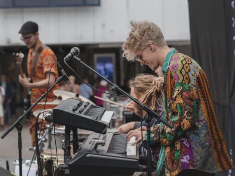 Iloinen nuori mies värikkäässä paidassa soittaa kosketinsoitinta.