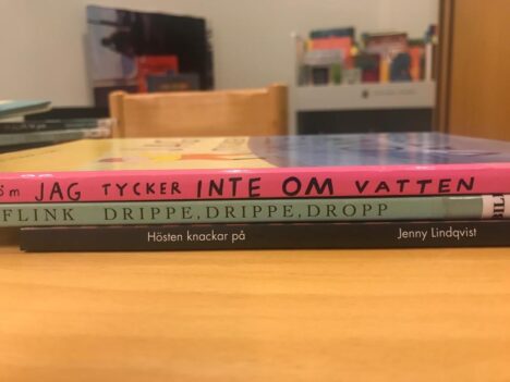 Tre böcker i en hög på ett bord. Bokryggarnas titlar bildar dikten "Jag tycker inte om vatten / Drippe drippe dropp / Hösten knackar på."
