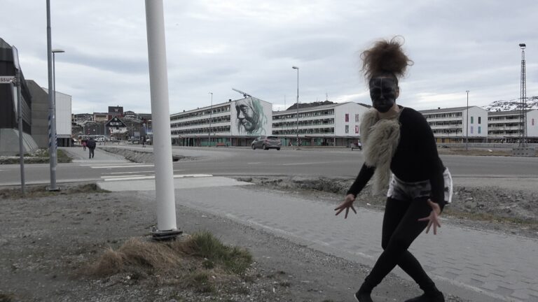 En traditionell Grönländsk maskdansare sminkad och klädd i svart går på gatan i Nuuk i Grönland