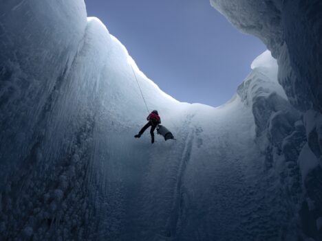 A man is rappelling into a glacier