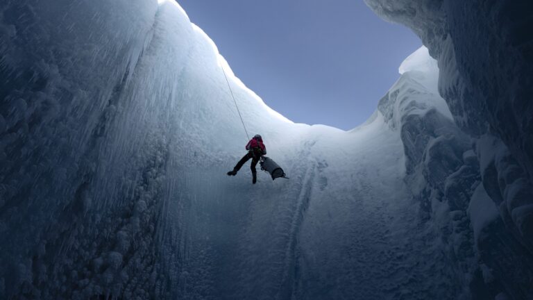 A man is rappelling into a glacier