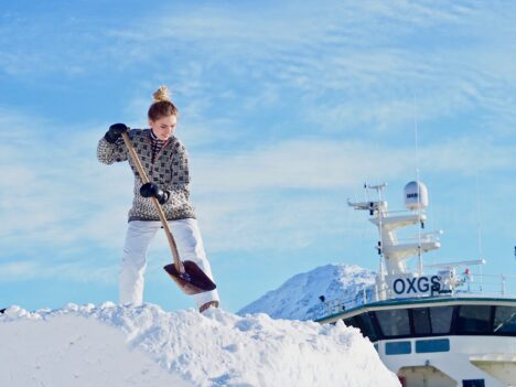 Kvinna står uppe på en stor snöhög och skyfflar snö.