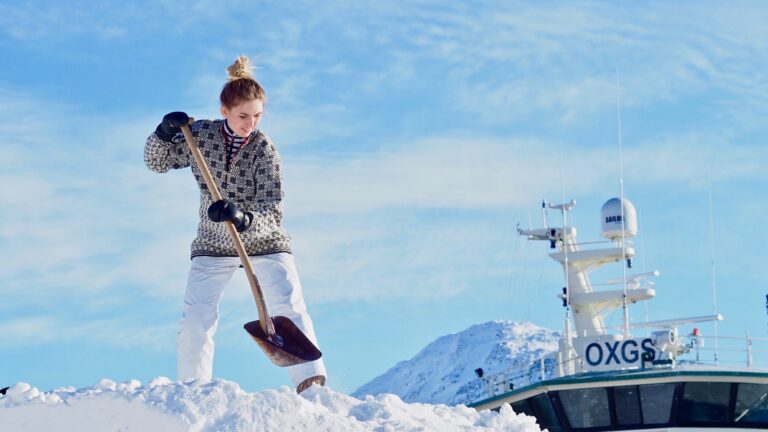 Kvinna står uppe på en stor snöhög och skyfflar snö.