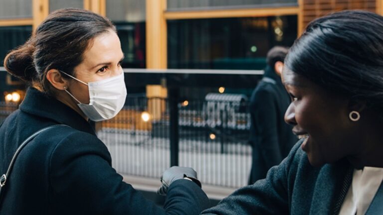 Two women with face masks greeting each other with their elbows.